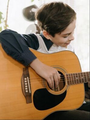 Picture of a kid playing guitar. We post this picture because we offer kids guitar lessons and we are hoping to start offering guitar classes soon.
