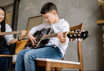 The student in this picture is learning jazz, pop, and blues on the guitar. It looks like he is playing an acoustic-electric guitar